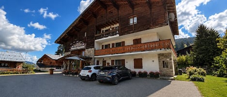 Ein zweistöckiges Holzhaus mit Balkon und überdachter Sitzgruppe, vor der ein Auto parkt.