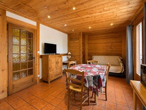 A cozy room with a wooden ceiling, a television on a wooden cabinet, a quilted bed, and a tiled floor. - Charming apartment in the center, near the slopes (Crest-Voland)