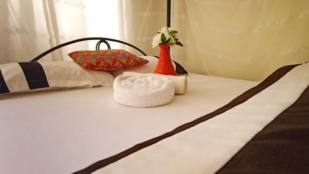 A neatly made bed with a striped bedspread, a white pillow, and a decorative vase with a flower. - Cosmos Haven Studio (Kisumu)