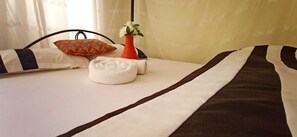 A neatly made bed with a striped bedspread, a white pillow, and a decorative vase with a flower. - Cosmos Haven Studio (Kisumu)
