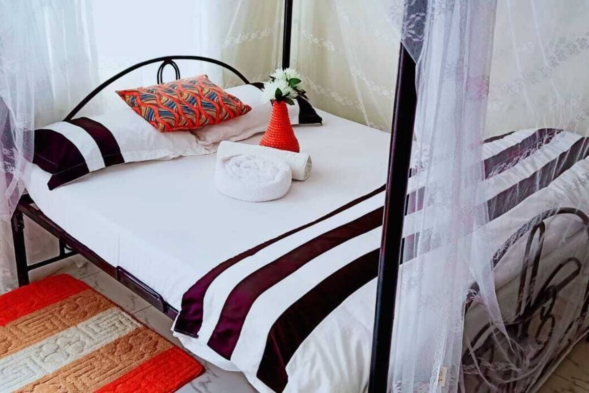 A bed with a mosquito net, a pillow, a vase with a flower, and a towel.