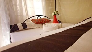A neatly made bed with a striped bedspread, a white pillow, a decorative pillow, and a small red vase with flowers. - Cosmos Haven Studio (Kisumu)