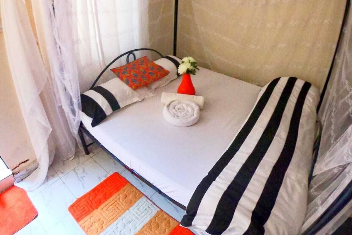 A single bed with striped bedding, a rolled towel, a small potted plant, and a decorative pillow.