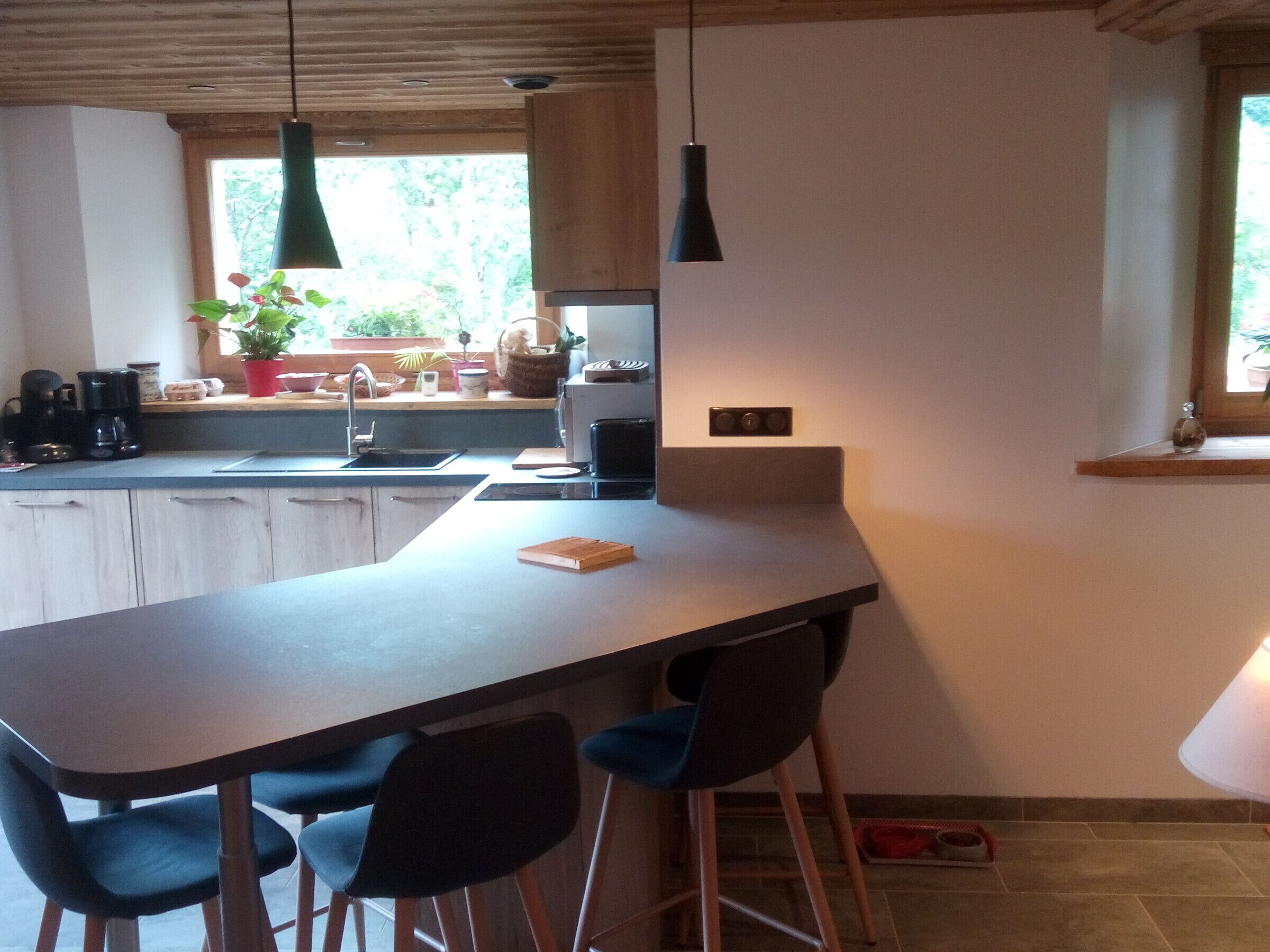 A modern kitchen with a long countertop, wooden cabinets, and a window with a view of greenery.