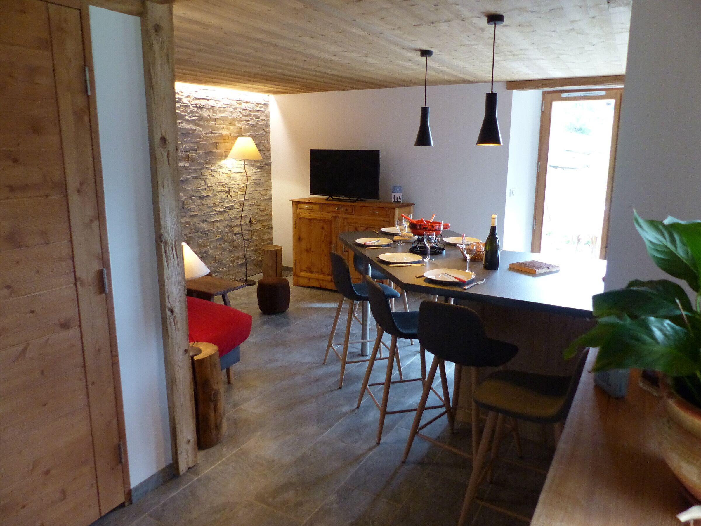 Eine moderne Küche mit Essbereich, Holzschränken, einer Steinwand und einem Fernseher.