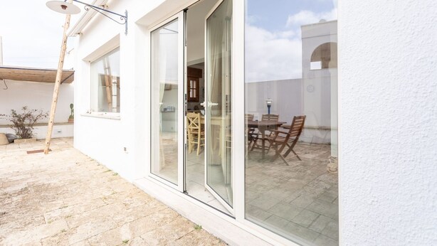 Ein modernes Haus mit Glastür, die auf eine Terrasse mit Tisch und Stühlen führt.
