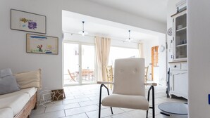 Ein Wohnzimmer mit einer Couch, einem Sessel, einem Esstisch mit Stühlen, einer Küchenzeile mit Schränken und einer Glastür zu einer Außenpatio.