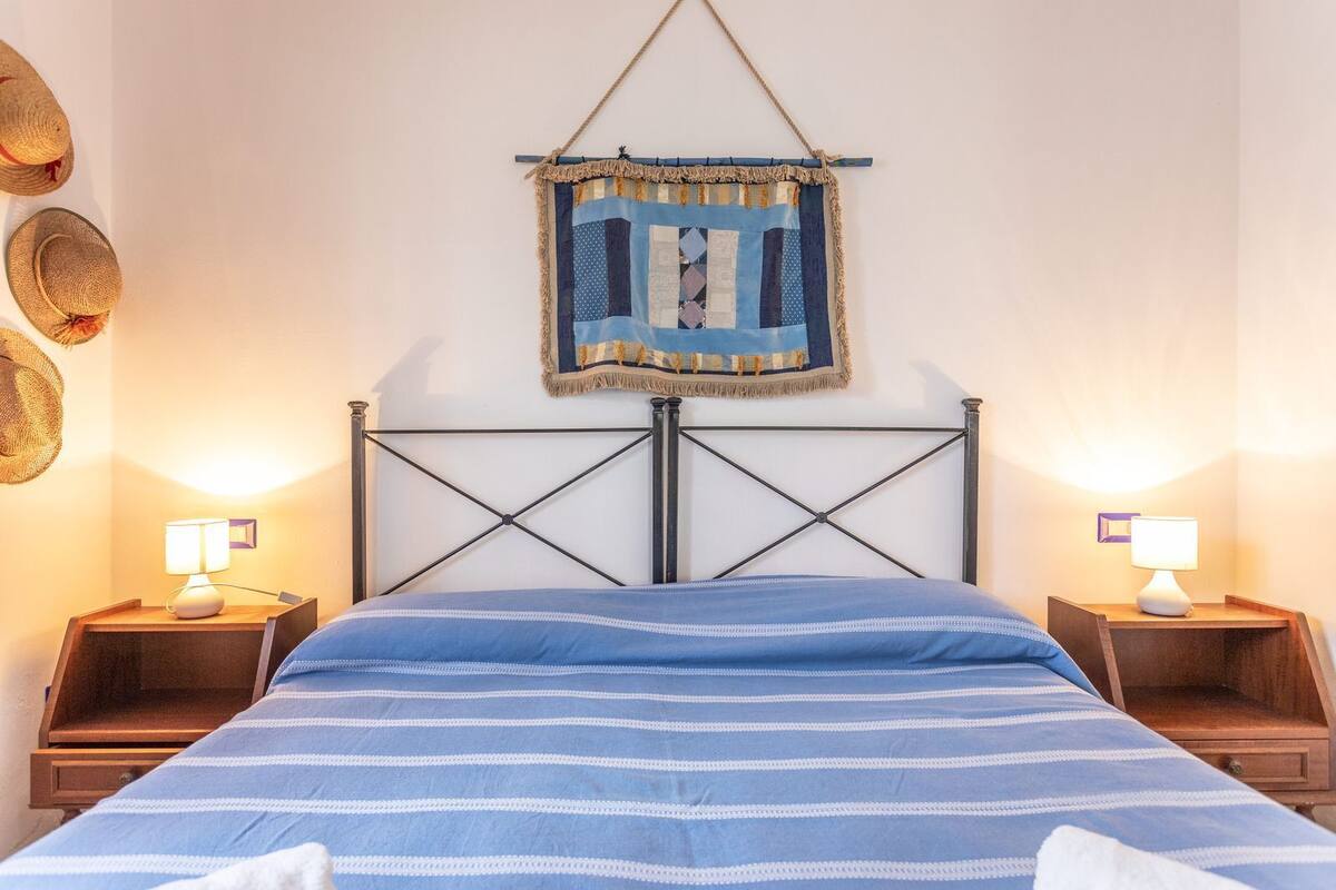 A bed with a blue and white striped bedspread, two bedside tables with lamps, and a wall hanging above the bed.