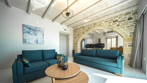 Ein geräumiges Wohnzimmer mit zwei Sofas, einem Holztisch und einem steinernen Bogen, der in eine Küche führt.