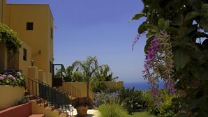 Un edificio in stile mediterraneo con una scala in pietra che conduce a un balcone, circondato da vegetazione lussureggiante e piante fiorite.