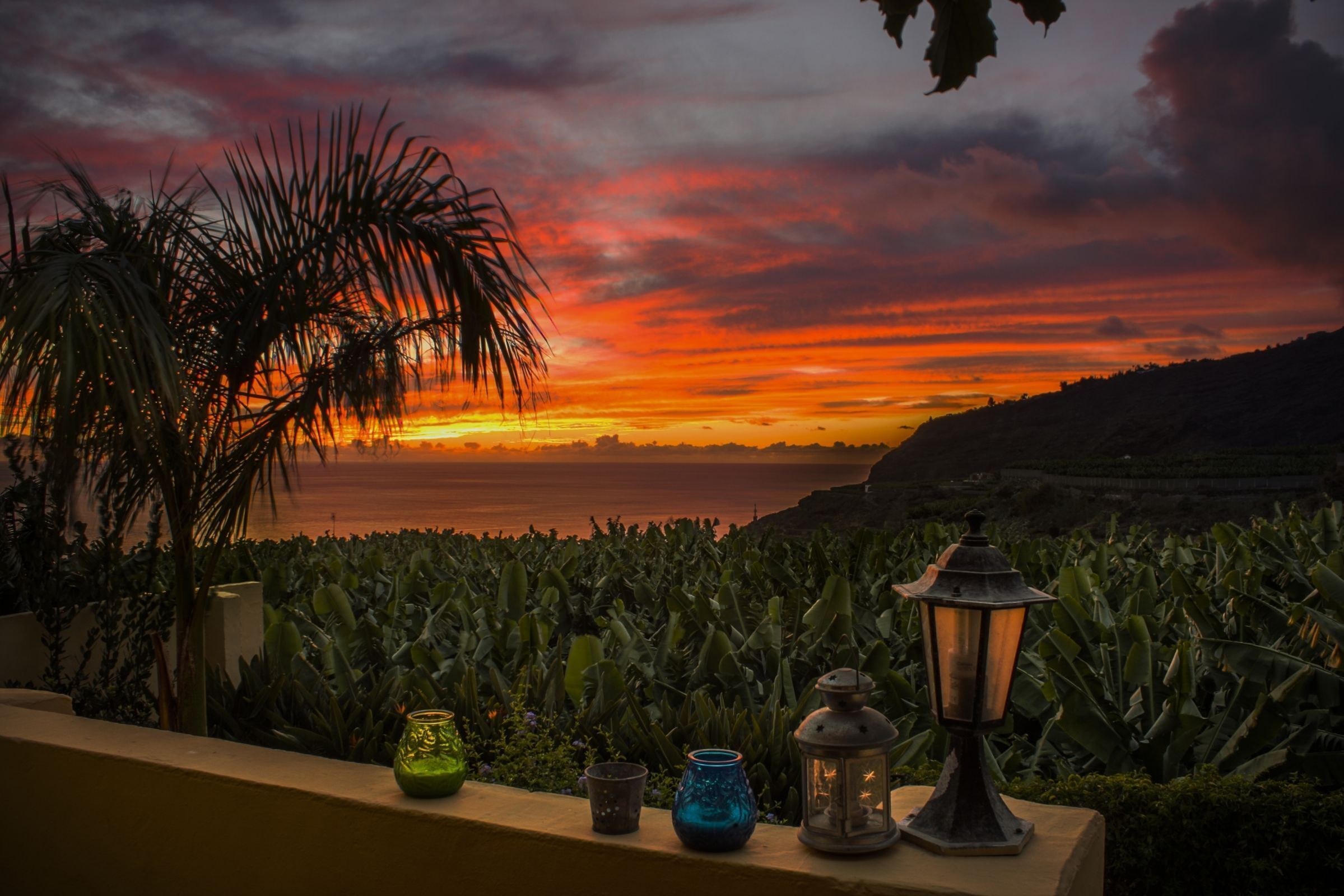 A sunset view from a balcony with a row of decorative vases and a lantern.