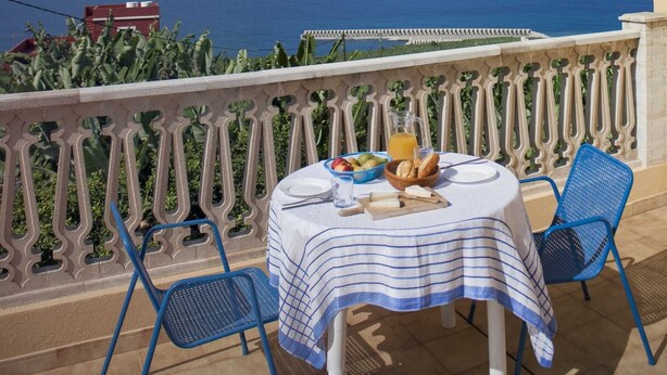 A terrace with a table set for two, overlooking a coastal view.