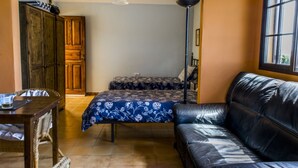 A room with a bed, a leather sofa, a wooden wardrobe, a table with a chair, and a floor lamp.