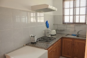 A kitchen with white tiles, a gas stove, a coffee maker, and wooden cabinets.