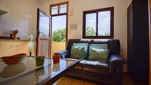 Un espacio habitable compacto con kitchenette, una mesa de vidrio, un sofá de cuero con cojines, y vistas a través de un ventanal.
