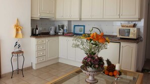 A kitchen with white cabinets, a microwave, a coffee maker, a small table with a vase of flowers, and a decorative sailboat.