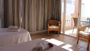 A hotel room with two beds, a wicker chair, and a balcony with a railing.
