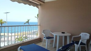 Un balcone con vista sull'oceano, un tavolo, due sedie e una poltrona da relax.