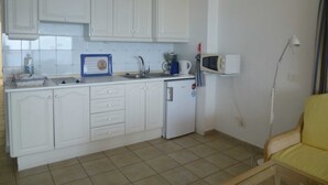 Una cucina compatta con mobili bianchi, un piccolo frigorifero, un forno a microonde e un lavandino.
