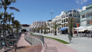 Una passeggiata costiera con palme, un percorso in legno curvo e moderni edifici con balconi.