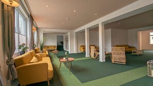 A spacious lobby with yellow sofas, a green carpet, and wicker furniture. - Lieblingsplatz Hotel Wannerhus (Groemitz)