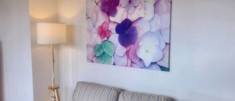 A living room with a striped sofa, a floor lamp, and a floral wall art piece.