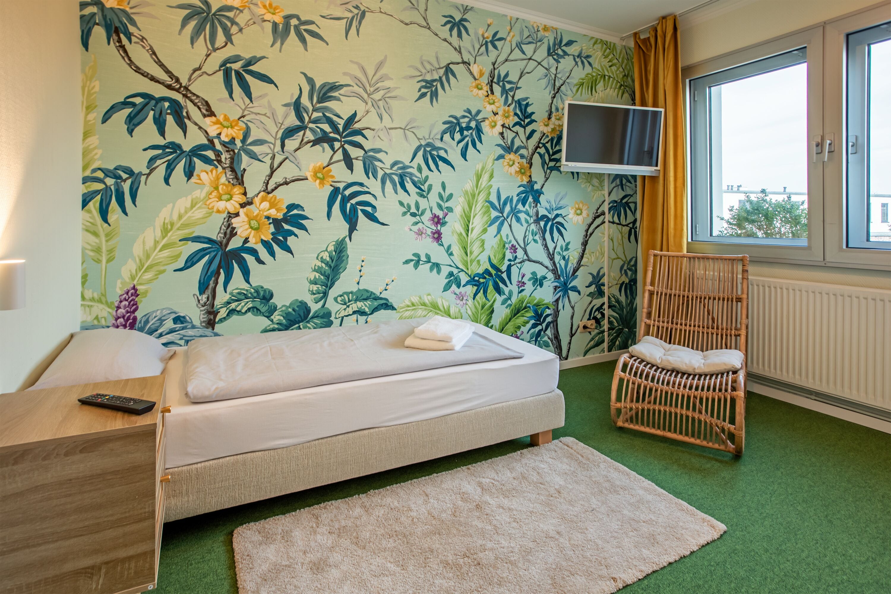 Ein Zimmer mit Bett, Fernseher an der Wand, Fenster und Stuhl.