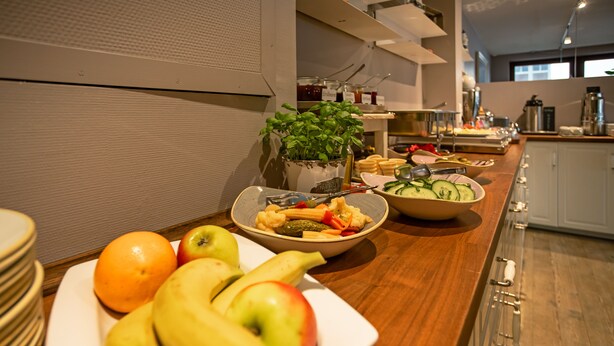 A buffet table with various fruits and vegetables, a potted plant, and kitchen appliances in the background. - Lieblingsplatz Hotel Wannerhus (Groemitz)