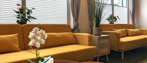 A modern living room with a yellow sofa, a round coffee table with a plant, and large windows with curtains.