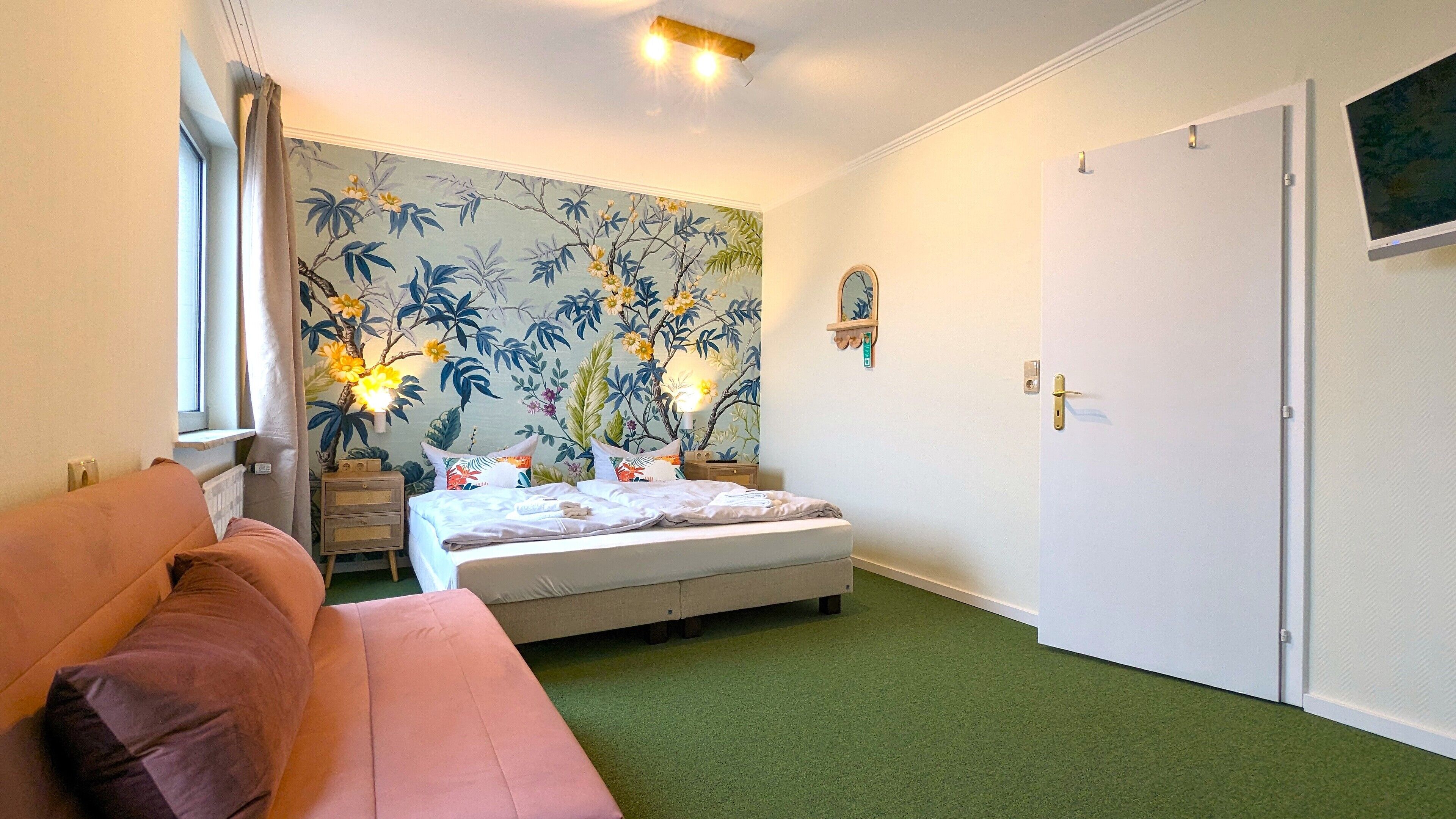 Ein Schlafzimmer mit einem Bett, einem Nachttisch, einer Lampe, einem Fenster mit Vorhängen, einer Tür und einem grünen Teppich.