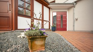 A building entrance with a gravel pathway, a wooden door, and a red door in the background. - Lieblingsplatz Hotel Wannerhus (Groemitz)