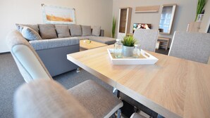 A modern living room with a grey sofa, a wooden dining table with a tray, and a television in the background. - Lieblingsplatz Hotel Wannerhus (Groemitz)