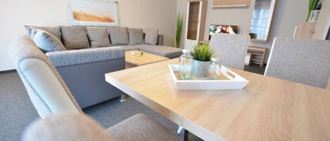 Ein modernes Wohnzimmer mit einem grauen Sofa, einem Holztisch mit Tablett und einem Fernseher im Hintergrund.