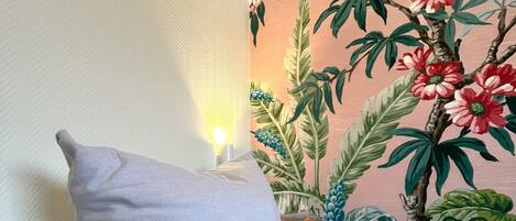A sofa with two pillows, one plain and one with a floral pattern, against a wall with a tropical mural.