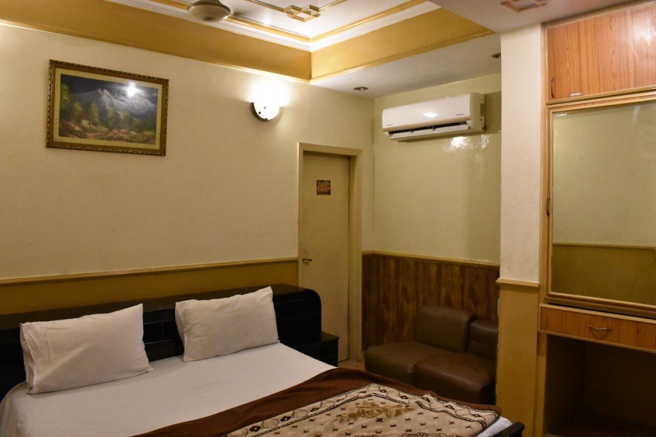 Een hotelkamer met een bed, een stoel, een airconditioner en een houten garderobe.