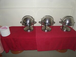 A table with three covered food service stations, each with a dome lid and two handles, set on a red tablecloth.