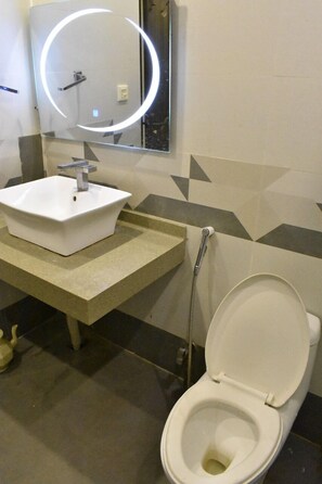 A bathroom with a white sink, a mirror with a circular light, and a toilet.