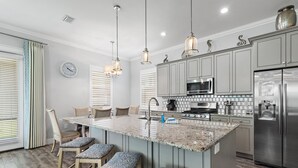 Una cucina con isola centrale, sgabelli da bar, forno a microonde, frigorifero e illuminazione a sospensione.