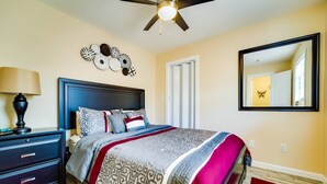 A bedroom with a bed, a nightstand, a lamp, a ceiling fan, a wall-mounted mirror, and a decorative wall piece. - Small 2BR / Fully Equipped Kitchen / Parking (Fort Lauderdale)