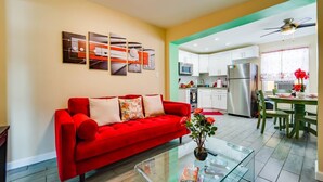 A modern living room with a red sofa, a glass coffee table, and a kitchen area with white cabinets and a stainless steel refrigerator. - Small 2BR / Fully Equipped Kitchen / Parking (Fort Lauderdale)