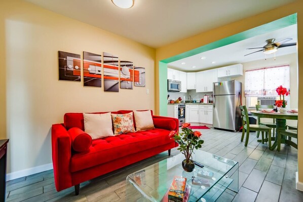 A modern living room with a red sofa, a glass coffee table, and a kitchen area with white cabinets and a stainless steel refrigerator. - Small 2BR / Fully Equipped Kitchen / Parking (Fort Lauderdale)