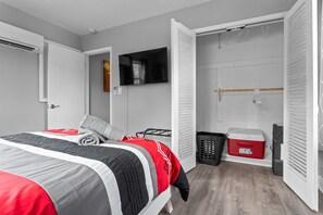 Ein Schlafzimmer mit Bett, Wandfernseher, Kleiderschrank mit Kleiderstange und Wäschekorb.
