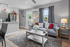 Ein modernes Wohnzimmer mit grauem Sofa, einem Couchtisch und einer Küchenzeile mit Kühlschrank und Schränken.