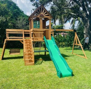 Une aire de jeux en bois avec un toboggan, une échelle d’escalade et une petite structure ressemblant à une maison.