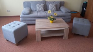 A living room with a grey sofa, two grey ottomans, a wooden coffee table, and a vase with yellow flowers. - Vacation apartment 3 - Rügen-Fewo 155 (Bergen auf Rügen)