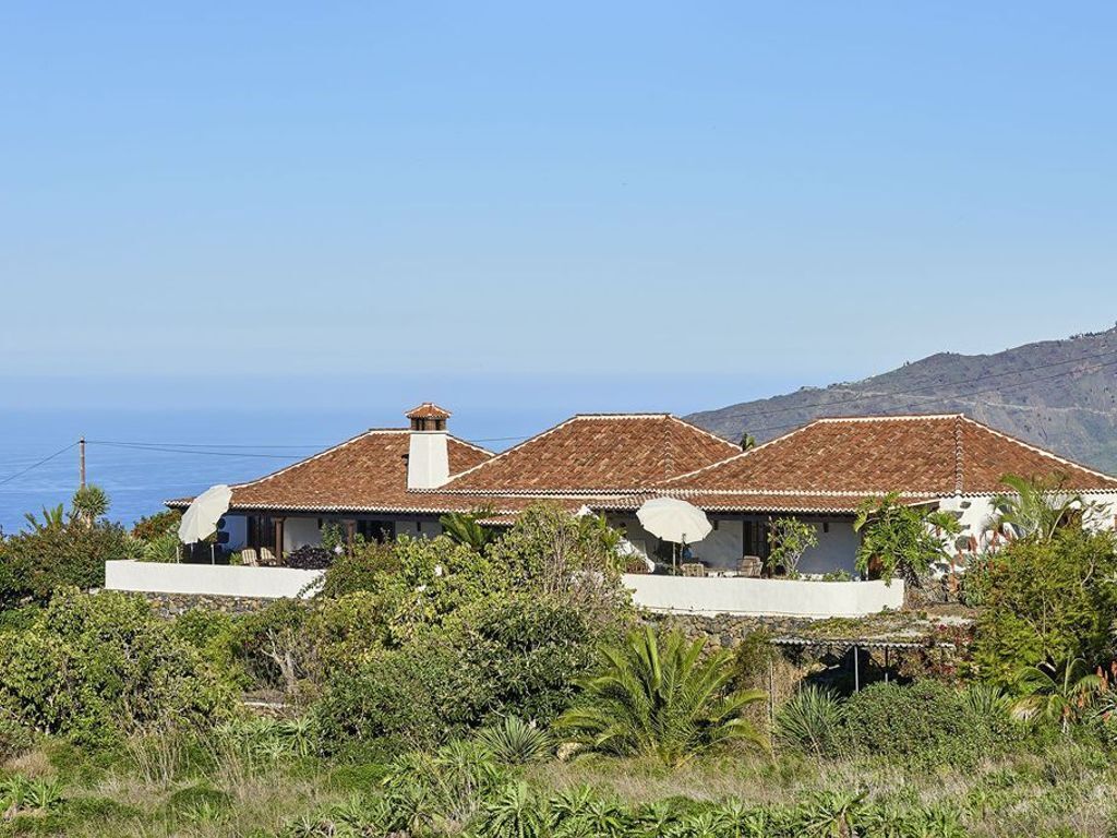 A coastal house with a tiled roof, satellite dishes, and a view of the sea.