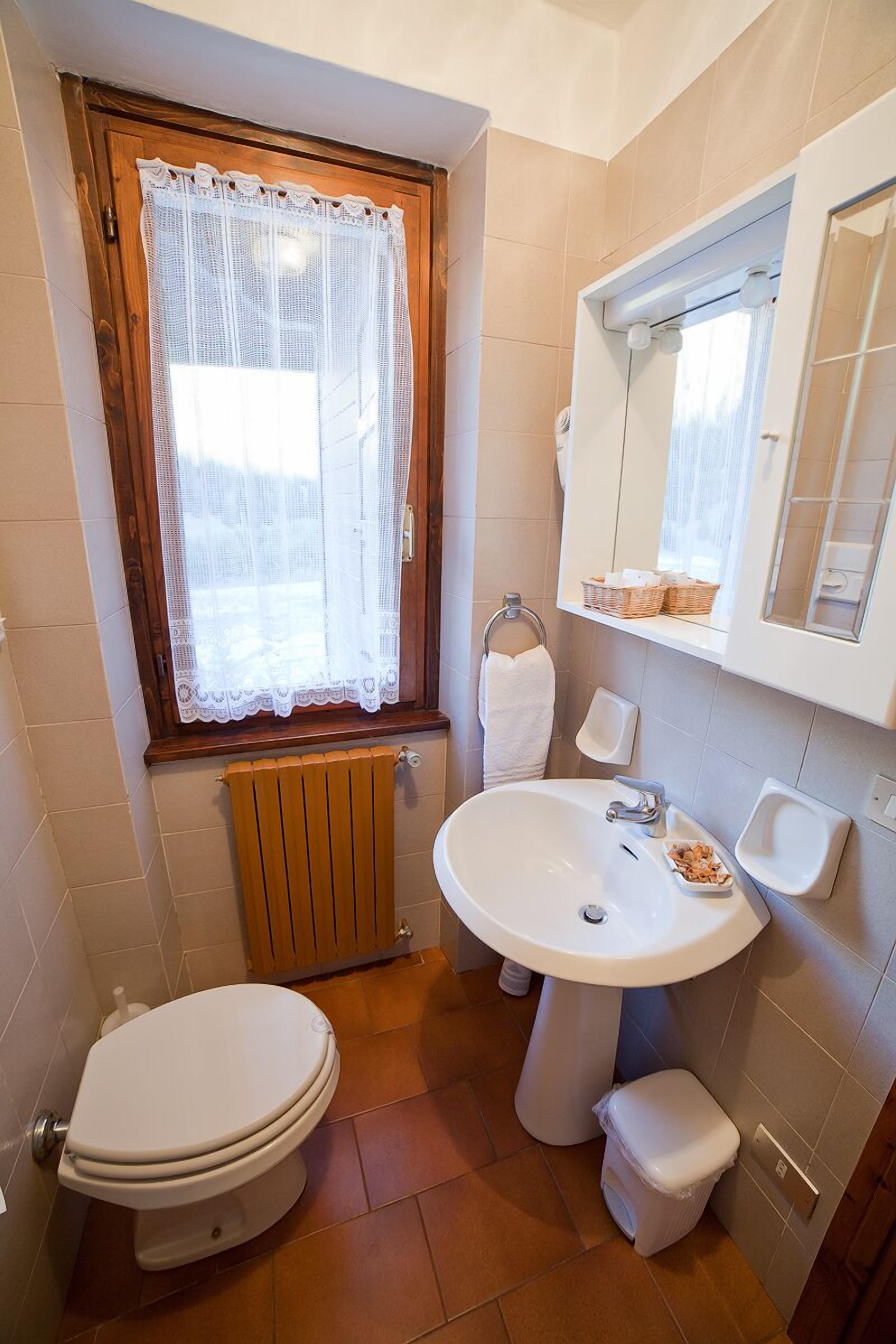 Ein Badezimmer mit Toilette, Waschbecken und Fenster mit Spitzenvorhängen.