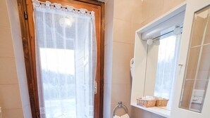 Een badkamer met toilet, wastafel en raam met kantgordijnen.