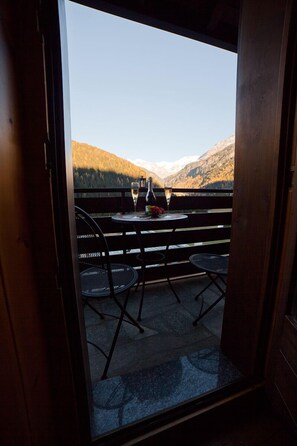 A balcony with a table set for two, featuring a bottle and glasses, overlooking a mountainous landscape. - ONE-ROOM APARTMENT ROMANTIC CHALET RELAXATION AND SPA (Santa Caterina Valfurva)