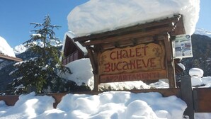 Een houten bord met de tekst 'CHALET BUCANEVE APPARTAMENTI' in een bergachtig gebied met sneeuw.